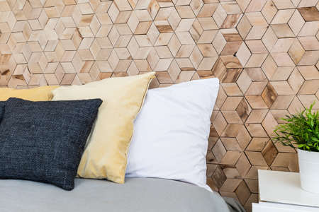 Bed with many pastel pillows in eco-friendly minimalist bedroom with wooden wallの写真素材