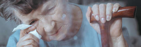 Older woman with dementia holding walking stick crying wiping tearsの写真素材
