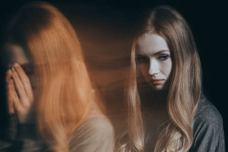 Young, sad woman with mental disorder covering her faceの写真素材