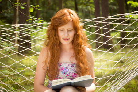 Ginger woman reading a book on a hammock in the gardenの写真素材