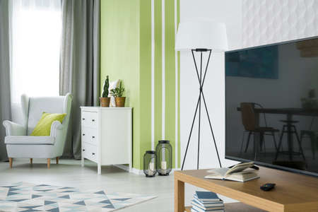 Green and white living room with tv, dresser and armchair