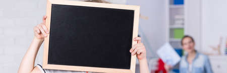 Small child holding a blackboard and covering his face with it