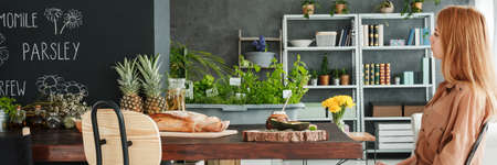 Woman sitting in modern kitchen with herbs and healthy foodの写真素材