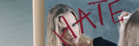 Young woman writing 'hate' on a mirror with her lipstickの写真素材