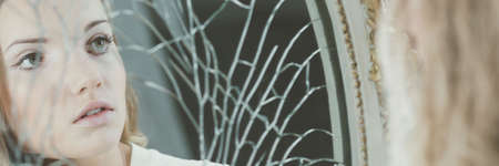 Young beautiful woman's face reflection in broken mirrorの写真素材