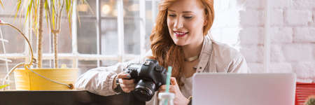 Young graphic designer holding a camera and working on her laptopの写真素材