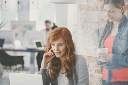 Smiling partners cooperating in co-working space looking at computerの写真素材