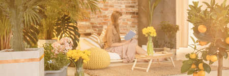 Young woman reading a book in living room full of plantsの写真素材