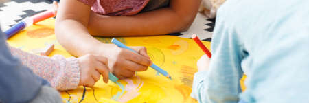 Little kids drawing pictures with crayons on yellow paperの写真素材