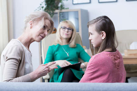Worried mother talking to troubled teenage girl during psychological visitの写真素材