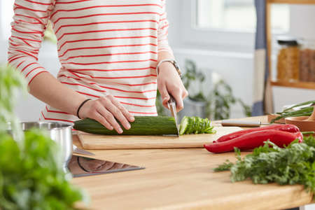 Woman cutting a cucumber on wooden table in a kitchenの写真素材