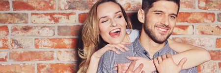 Young fashionable couple in love playing and flirting against brick wallの写真素材