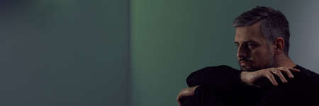 Glum man after divorce sitting alone in dark interior, panoramaの写真素材