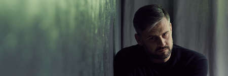 Glum man coping with depression, sitting in dark interior, panoramaの写真素材