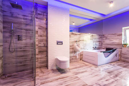Spacious bathroom with marble tiles, toilet, hot tub and glass shower cabin