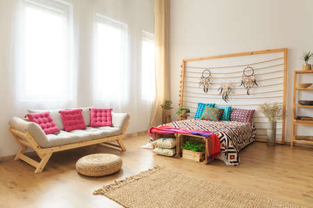 Photo of bed and couch standing in bright spacious bedroomの写真素材