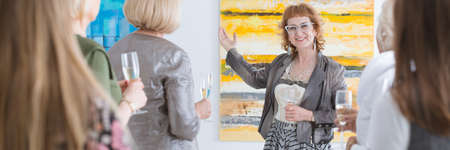 Senior elegant smiling woman presenting painting during art showの写真素材