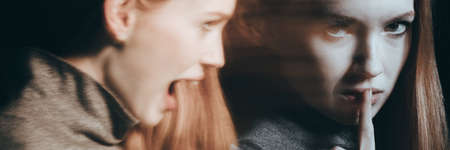 Young woman with schizophrenia with her finger on the mouthの写真素材