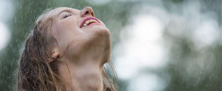 Young happy woman enjoying warm rain during summer