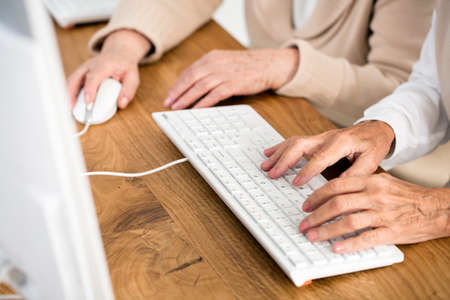 Close-up of two seniors' hands on keyboard and mouseの写真素材