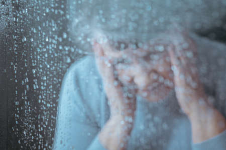 Sad lonely older woman behind the glassの写真素材