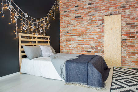 Simple bed with DIY headboard in stylish minimalist bedroom with brick wall