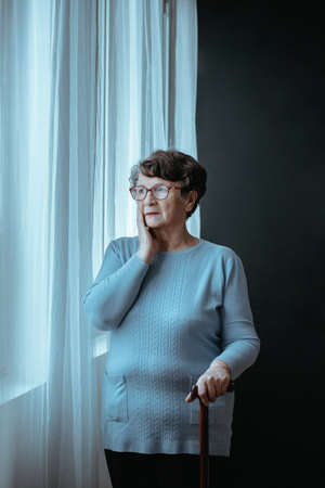 Older lady standing by the window with a stickの写真素材