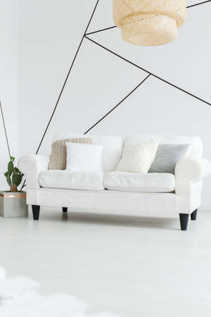 Big wooden lampshade hanging above white comfy sofa