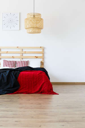 Wooden bed with red and black blankets in spacious bedroomの写真素材