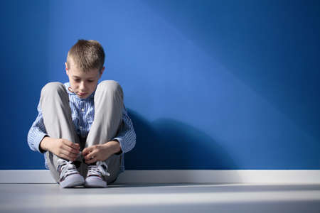 Depressed boy sitting on a floor in blue roomの写真素材