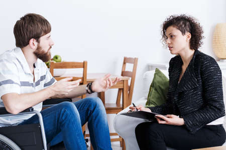 Young disabled man talking to female psychologist at home