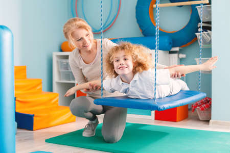 Woman helping a smiling boy to exercise on a therapy swingの写真素材