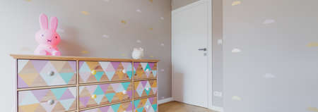 Little children's bedroom wth pink wallpaper and colorful commode with toys on itの写真素材