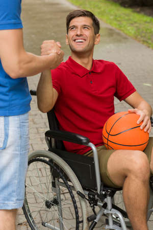 Happy disabled man holding a basketball, spending time in the park with his friendの写真素材