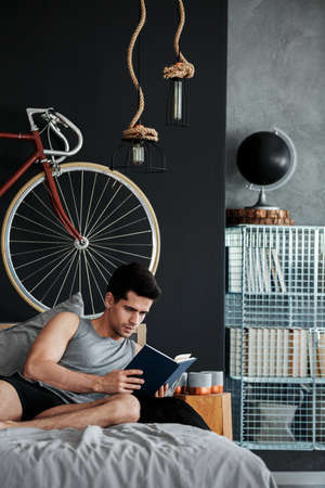 Handsome young man relaxing on a bed with book