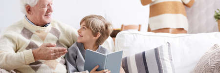 Grandpa and happy grandson sitting on a sofa, talking and reading