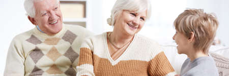 Loving grandparents sitting on a sofa and talking with a happy grandson