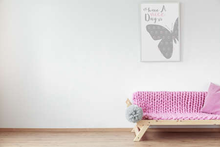White wall with positive poster and wooden couch with pink blanketの写真素材