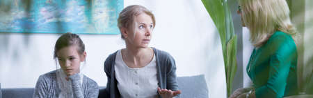 Middle-aged mother and teenage daughter talking during psychotherapy in officeの写真素材