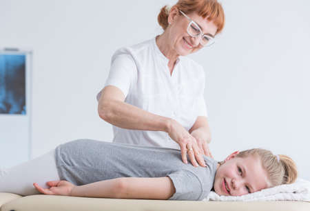 Girl lying on physiotherapy table and having back massage by chiropractorの写真素材
