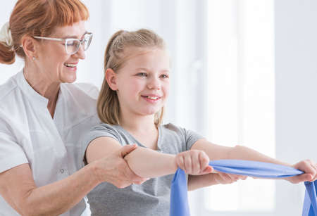 Young girl with physiotherapist exercising with rubber resistance band