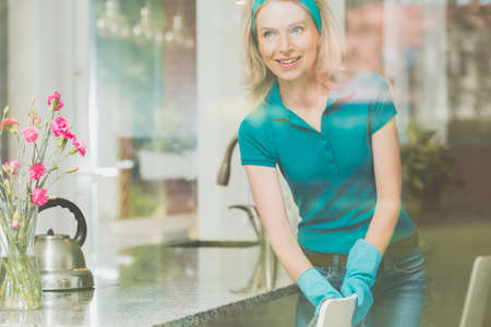 Happy blonde woman with blue band on head is cleaning in the kithen の写真素材