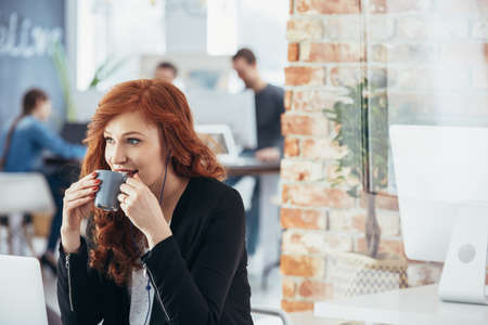 Beautiful young woman drinking coffee in modern officeの写真素材