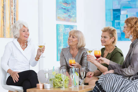 Four elder ladies talking and sitting with cocktailsの写真素材