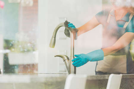 Girl cleans the kitchen stainless steel faucet using spongerの写真素材