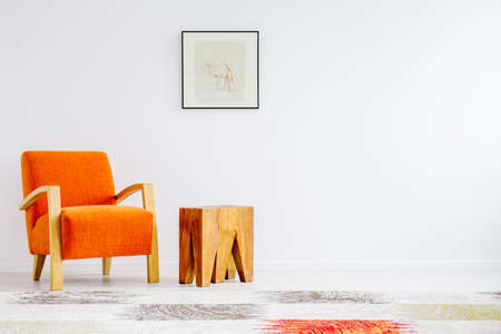 Trendy orange chair next to creative coffee table with bright picture above