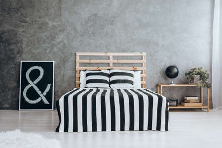 Black picture on the white glossy floor next to king-size bed with stripped coverletの写真素材