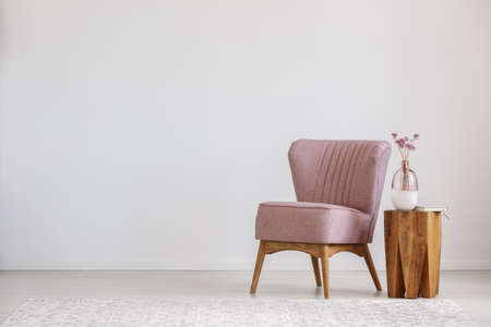 Cute pink flowers in glass vase placed on wooden table standing by small chairの写真素材