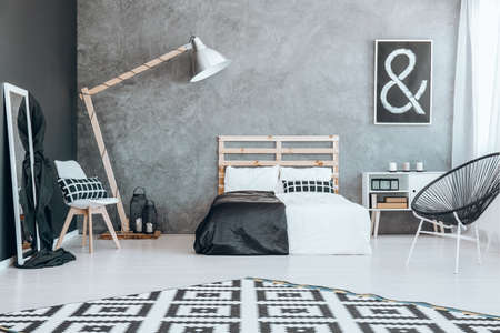 Wooden bed with black and white coverlet against concrete wallの写真素材