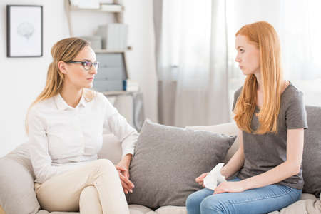 Mental health concept - young psychologist listening to female patient on a sofaの写真素材
